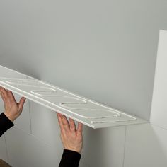 two hands are reaching up to the bottom of a shelf that is attached to a wall