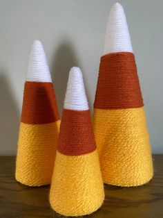 three knitted cones sitting on top of a wooden table with white and orange stripes