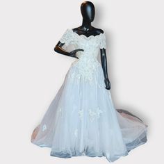 a mannequin wearing a white wedding dress with flowers on the skirt and sleeves