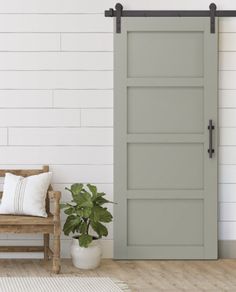 a room with a wooden bench and green sliding barn door in it, next to a potted plant