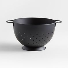 a black colander is sitting on a white surface and has holes in the bowl