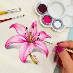 a woman is painting a pink flower with watercolors