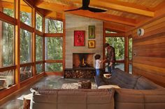 two people standing in a living room with wood paneling and large windows on the wall