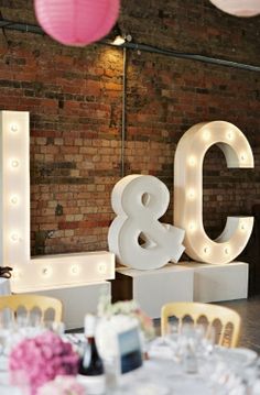 a table set up for a wedding reception with lights on the letters and tables in front of them