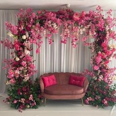 a couch sitting under a pink flower covered arch next to a white wall with flowers on it