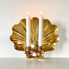 two candles are lit on a brass scallop