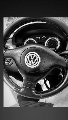 black and white photograph of the inside of a car steering wheel, dash board and dashboard