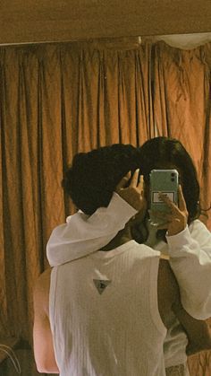 a man and woman taking a selfie in front of a mirror with curtains behind them