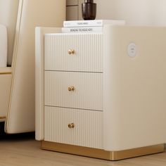 a white cabinet with gold handles and drawers in a room next to a bed, lamp and chair