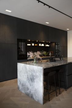 a large kitchen with marble counter tops and black cabinets, along with two bar stools