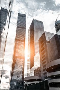 some very tall buildings in the middle of a big city with sun shining through them