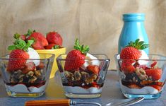 three dessert dishes with strawberries and granola in them on a table next to a blue bottle