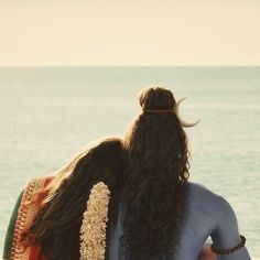 two women are sitting on the beach facing the ocean with their backs to each other