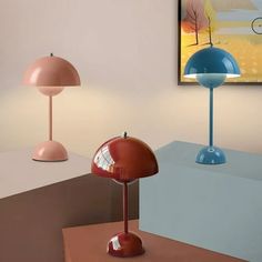 three different colored lamps sitting on top of a table next to each other in front of a painting