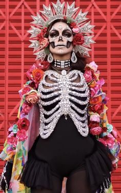 a woman in a skeleton costume with flowers on her head and arms, standing next to a red wall