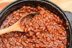 a wooden spoon in a black pot filled with baked beans on a wood table top