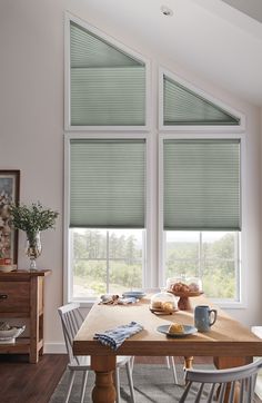 a dining room table and chairs with two windows in the background, all covered by shades