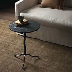 a small table with a book on it in front of a white couch and window