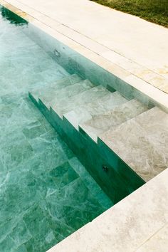 an empty swimming pool with steps leading up to the water's edge and grass in the background