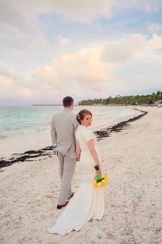 a bride and groom walking on the beach