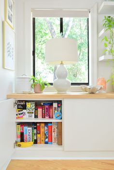 a white shelf with books and a lamp on it in front of a large window