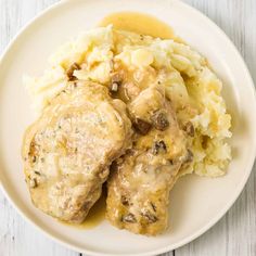 a white plate topped with meat covered in gravy and mashed potatoes on top of a wooden table