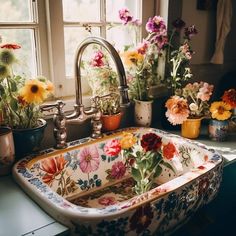 a sink that has some flowers in the bowl next to it and plants on the window sill