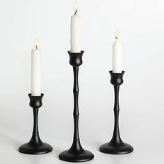 three black candlesticks with one white candle