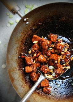 a pan filled with meat and nuts on top of a table next to a spoon