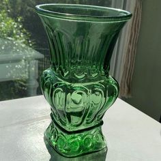 a green glass vase sitting on top of a table next to a window sill