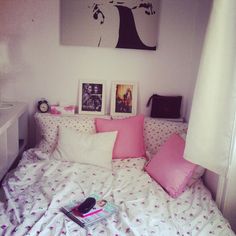 a white bed with pink pillows and pictures on the wall above it in a bedroom