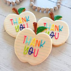 three decorated cookies with thank you written on them and two necklaces attached to the back