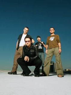 four men standing in front of a blue sky with one man wearing sunglasses and the other holding his hand on his hip