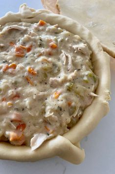 a pie crust filled with chicken and vegetables on top of a white table next to crackers