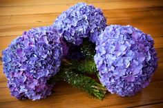 three purple flowers sitting on top of a wooden table