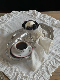 a cup of coffee and some blackberries on a silver tray with a white cloth