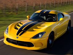 the yellow sports car is driving down the road with black stripes on it's hood