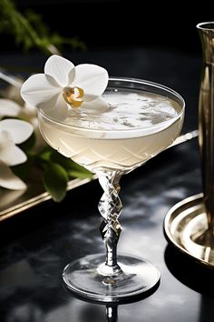 a white flower sitting on top of a table next to a glass filled with liquid