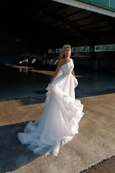 a woman in a white dress is standing on the sidewalk near an overpass and looking off into the distance