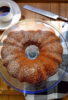 a bundt cake sitting on top of a glass plate next to a cup of coffee