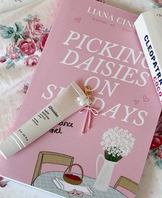 a pink book sitting on top of a bed next to a tube of lip balm