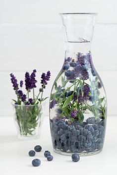 two vases filled with blueberries and flowers on top of a white table next to each other