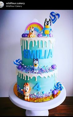 a three tiered cake with cartoon characters on the top and blue icing, sitting on a white pedestal