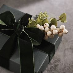 a gift wrapped in black paper with a green ribbon and bow on the top, sitting on a table