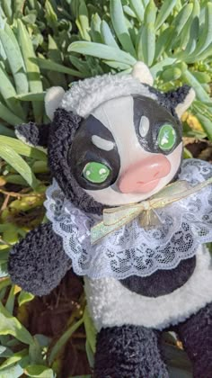 a black and white stuffed animal with green eyes sitting in the grass next to plants