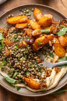 a plate filled with hummus, lentils and carrots on top of a wooden table