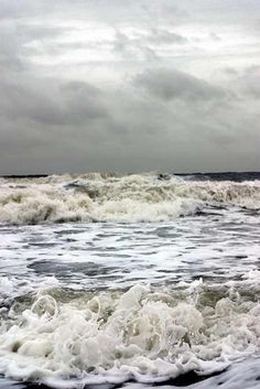 an ocean with waves crashing on the shore and dark clouds in the sky above it