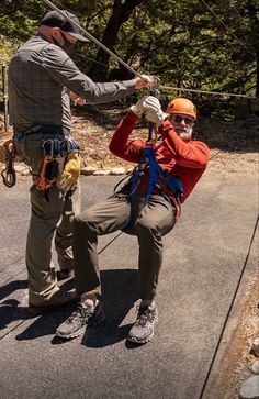 two men in safety gear holding onto ropes while standing on the side of a road