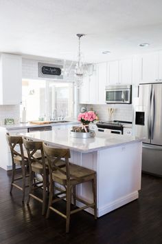 a kitchen with white cabinets and an island that has chairs around it in front of the sink