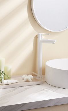 a white sink sitting next to a round mirror on top of a bathroom counter with candles